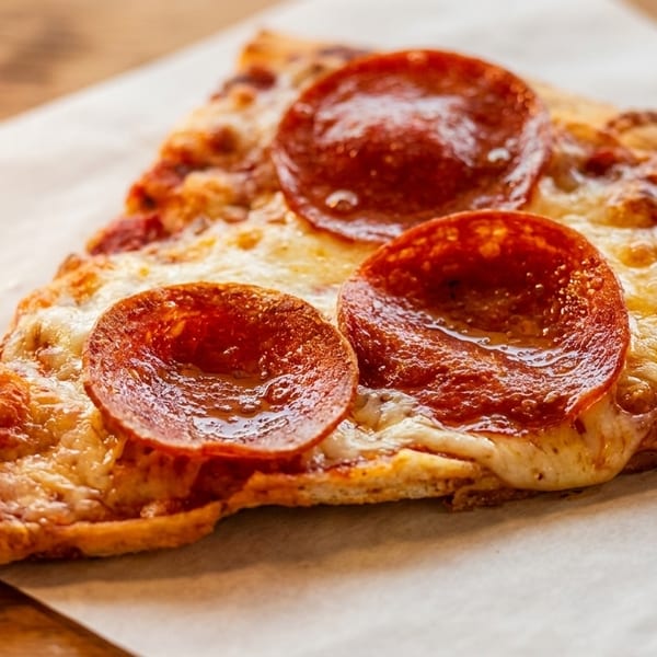 A single slice of pepperoni pizza with melted cheese on parchment paper.