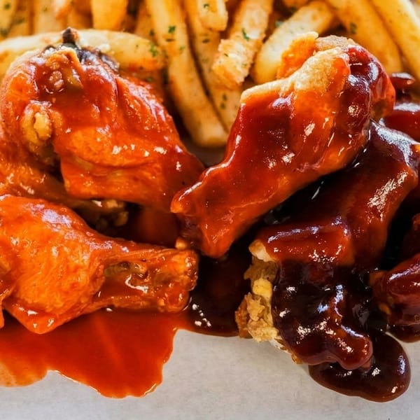 Chicken wings, some with red sauce and some with brown sauce, served with french fries.