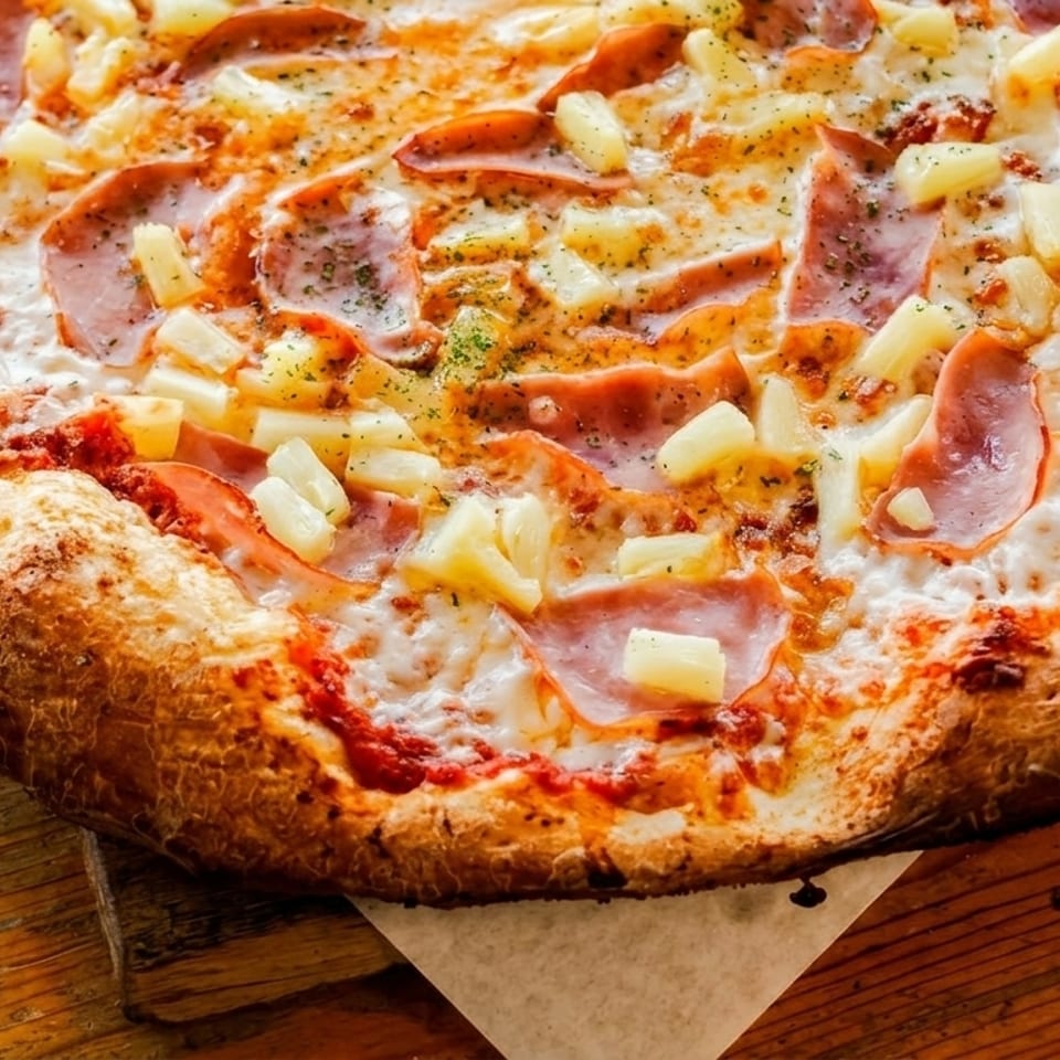 A Hawaiian pizza with ham and pineapple on a wooden board.