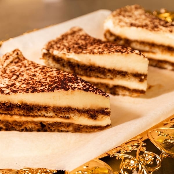 Three slices of tiramisu with cocoa powder on top, served on a decorative gold tray.